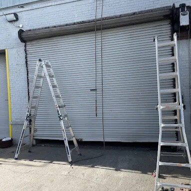 Commercial roll-up garage door repair with ladders set up in Brooklyn, NY