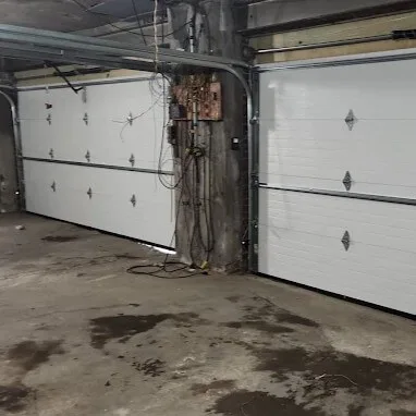White sectional garage doors installed inside an underground parking garage in Brooklyn, NY.
