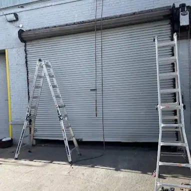 Commercial roll-up garage door repair with ladders set up in Brooklyn, NY